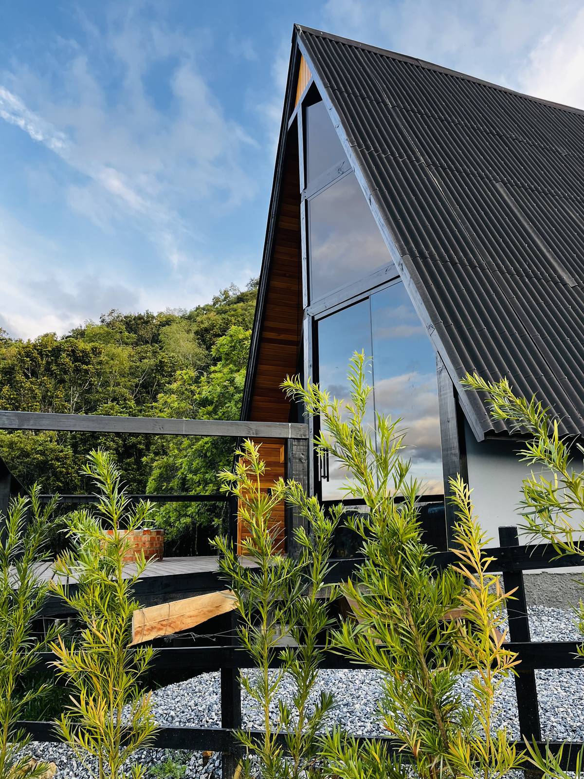 Fachada moderna do chalé em formato A-frame ao entardecer, com vegetação em primeiro plano