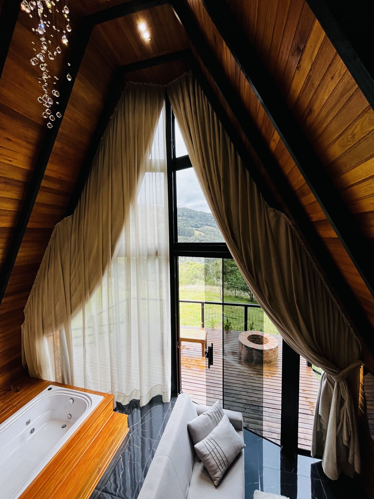 Hidromassagem com cortinas, lustre de cristal e vista panorâmica pela janela A-frame