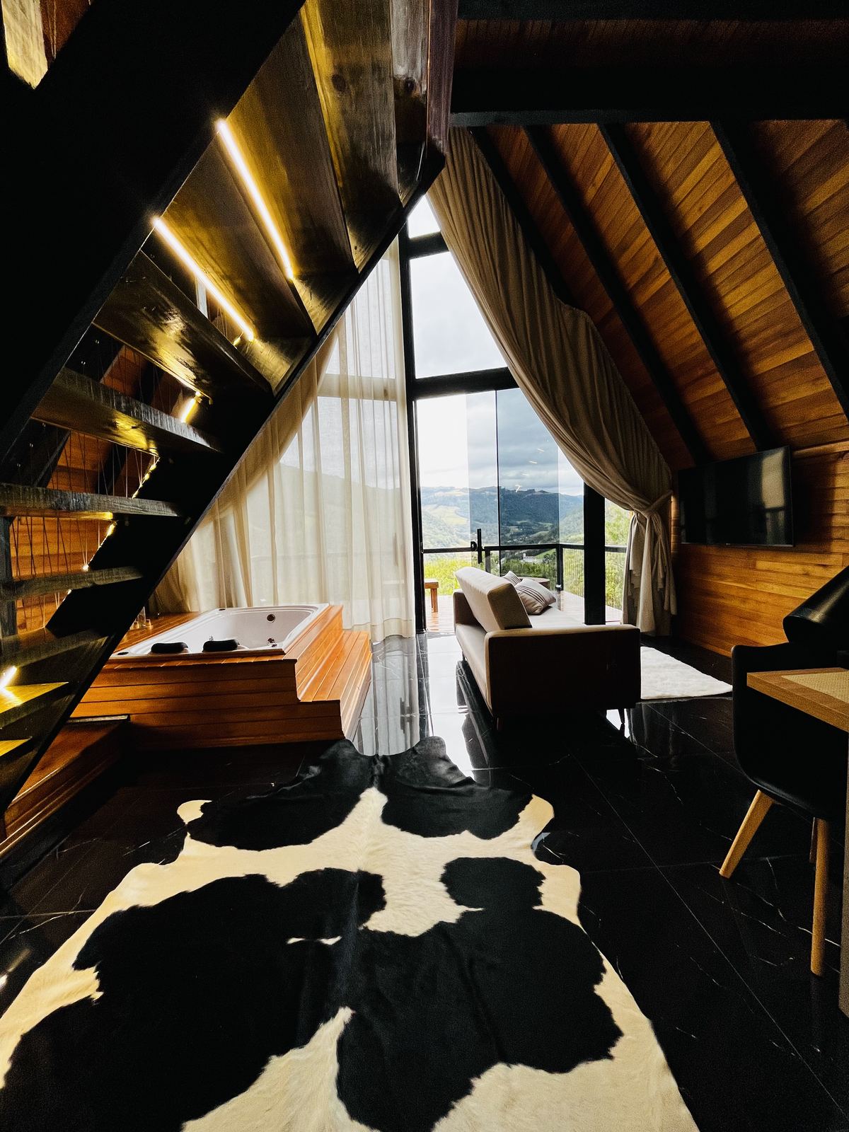 Escada de madeira e hidromassagem com tapete estilo zebra e TV ao fundo