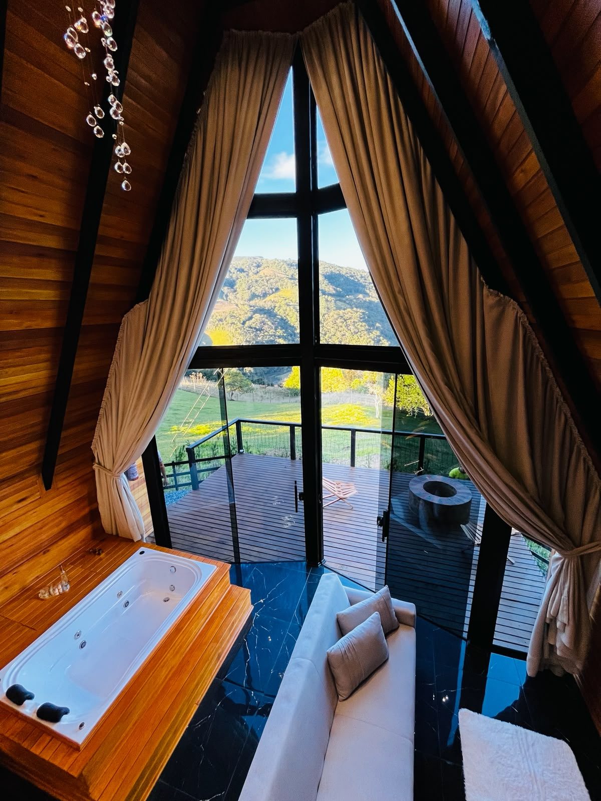 Interior do chalé com lustre de cristal, hidromassagem e vista para o campo