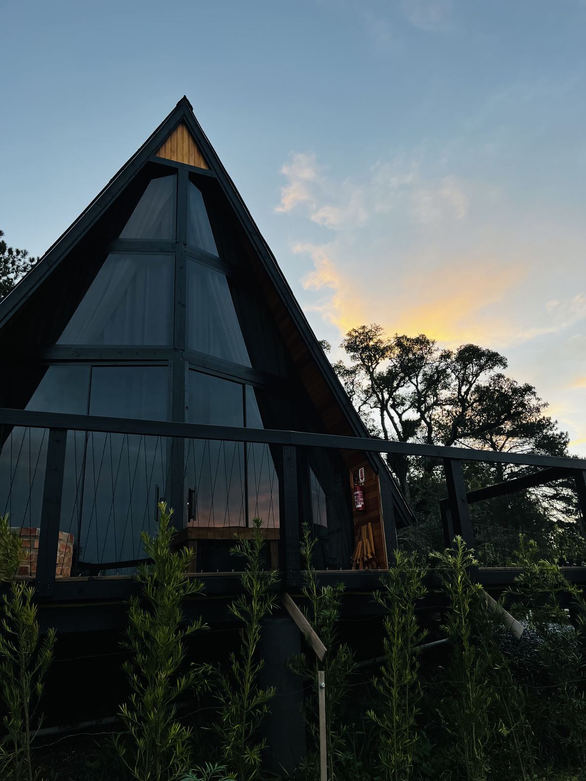 Fachada do chalé em formato A-frame ao anoitecer, com o céu colorido pelo pôr do sol