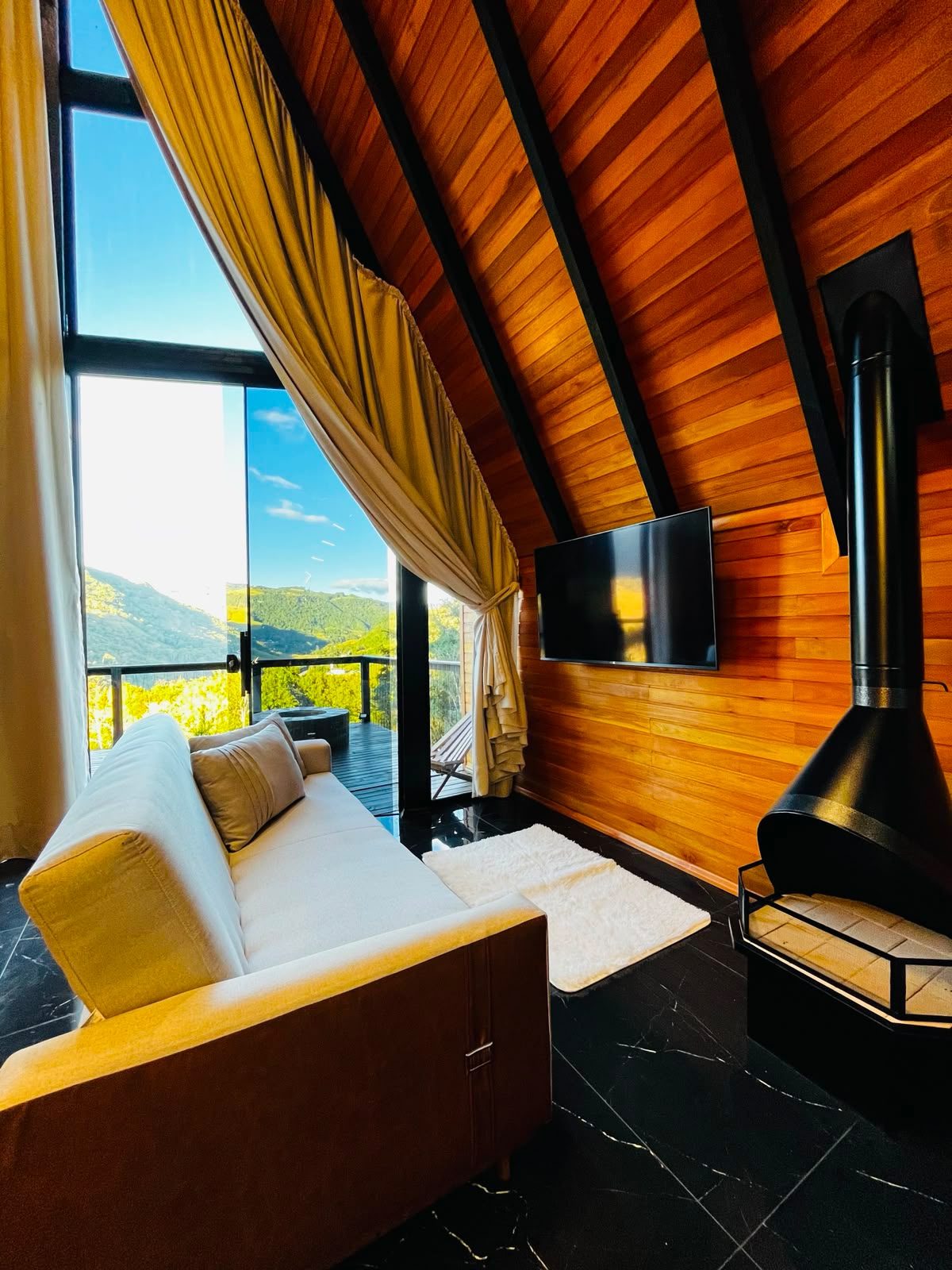 Sala de estar do Chalé Amanhecer da Serra com lareira, TV e vista panorâmica para as montanhas